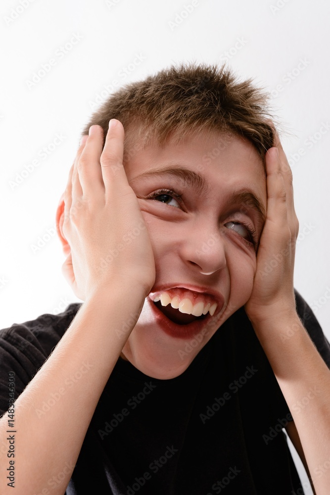 A boy laughs, holding his face in his hands. Joyful, playful expression. A boy laughs, holding his face in his hands. Joyful, playful expression.
