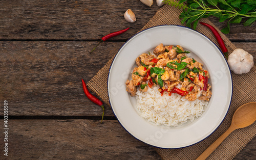 Top view of rice topped with stir fried chicken and basil in white plate on wooden background. Thai Food