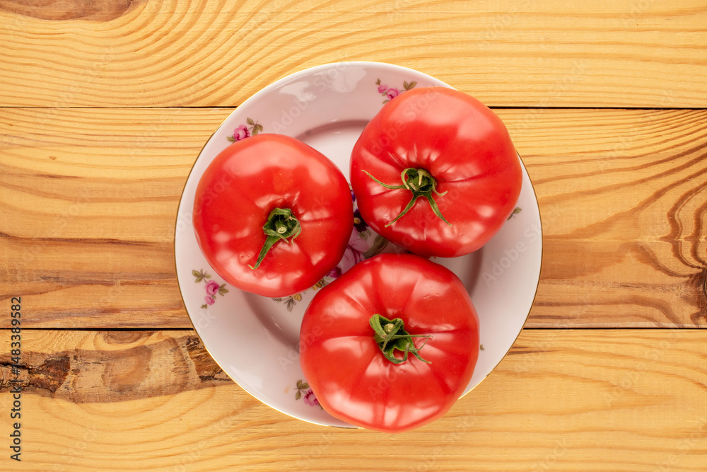 Three pink tomatoes with a ceramic plate on a wooden table, close-up, top view. Three pink tomatoes with a ceramic plate on a wooden table, close-up, top view.