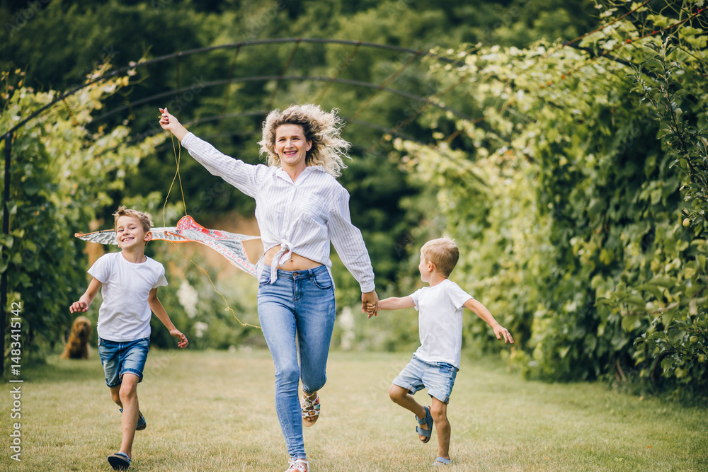 Fototapeta premium Mother and sons flying a kite. Happy Family day. Family flying a kite in a clearing near the forest.
