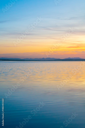 Sunset over a still lake with golden and blue tones reflecting in calm water. A peaceful and tranquil natural scene with a soft gradient sky.