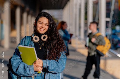 Smiling female university student holding notebooks, enjoying her return to school while embracing the vibrant campus atmosphere