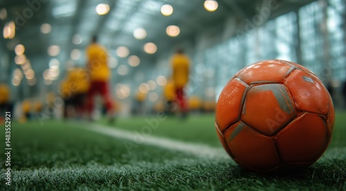 Bright Orange Soccer Ball on Green Turf With Players in Background During Ind...