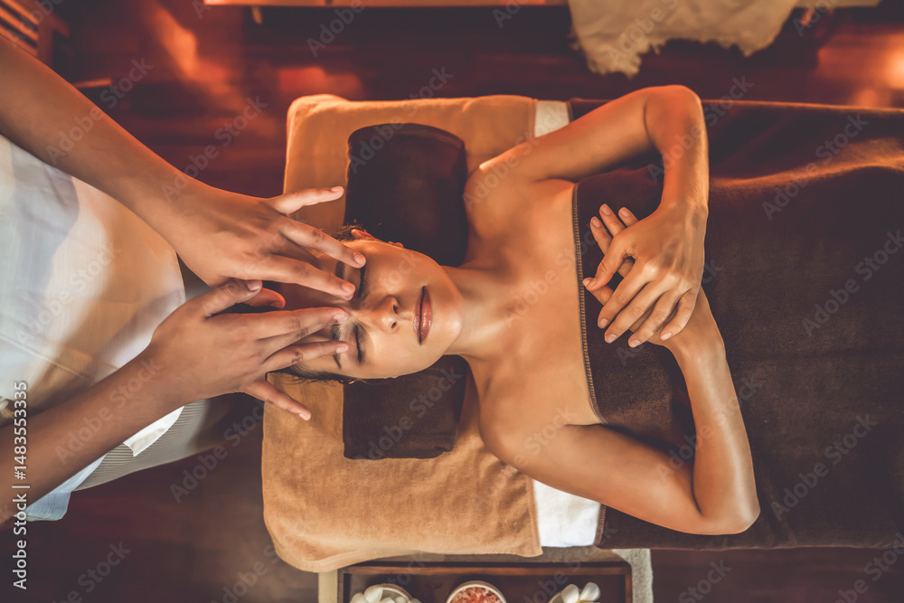 Fototapeta premium Caucasian woman enjoying relaxing anti-stress head massage and pampering facial beauty skin recreation leisure in warm candle lighting ambient salon spa in luxury resort or hotel. Quiescent