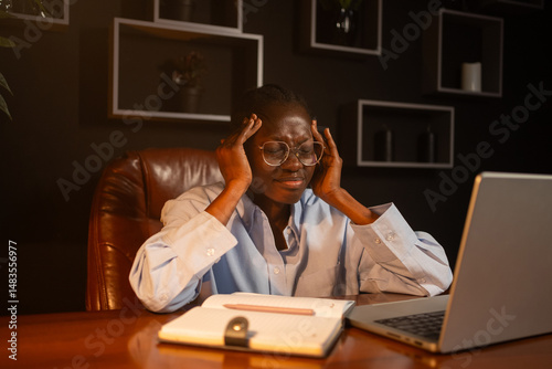 Quadro em tela Young african businesswoman struggling with a severe headache while working late