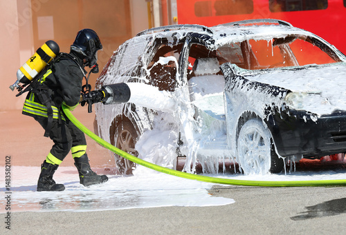 Firefighter with helmet and oxygen cylinder while operating   lance with   foam to extinguish   car fire after   road accident