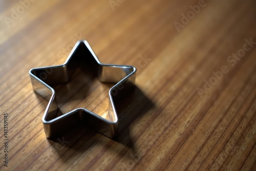 Shiny metal cookie cutter shaped like a star sits on a wooden surface , recipe, shape cutter, utensil