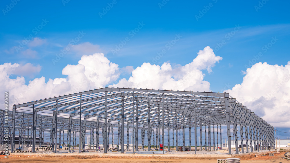 Fototapeta premium Large metal structure of factory warehouse industry buildings in construction site against clouds on blue sky background
