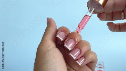 Moisturizing pink oil for cuticles. The woman cares for hands and nails, close up. Woman applying oil from pipette to cuticle on light background, macro. Healthy nails concept.