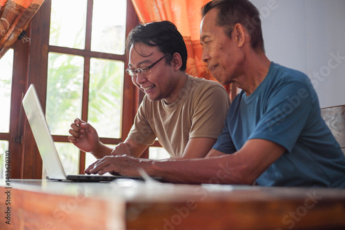 Happy adult son teaching old father using laptop. Young and senior togetherness concept