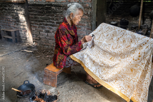 Indonesian woman making traditional batik fabric with canting tool photo