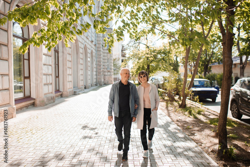 Senior happy couple of stylish man and woman 60-65 year old walking together on streets at city outdoors. Wellness lifestyle. Spring season.
