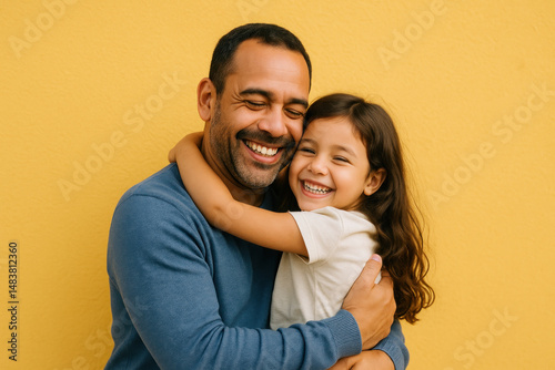Father embraces daughter in front of yellow wall.