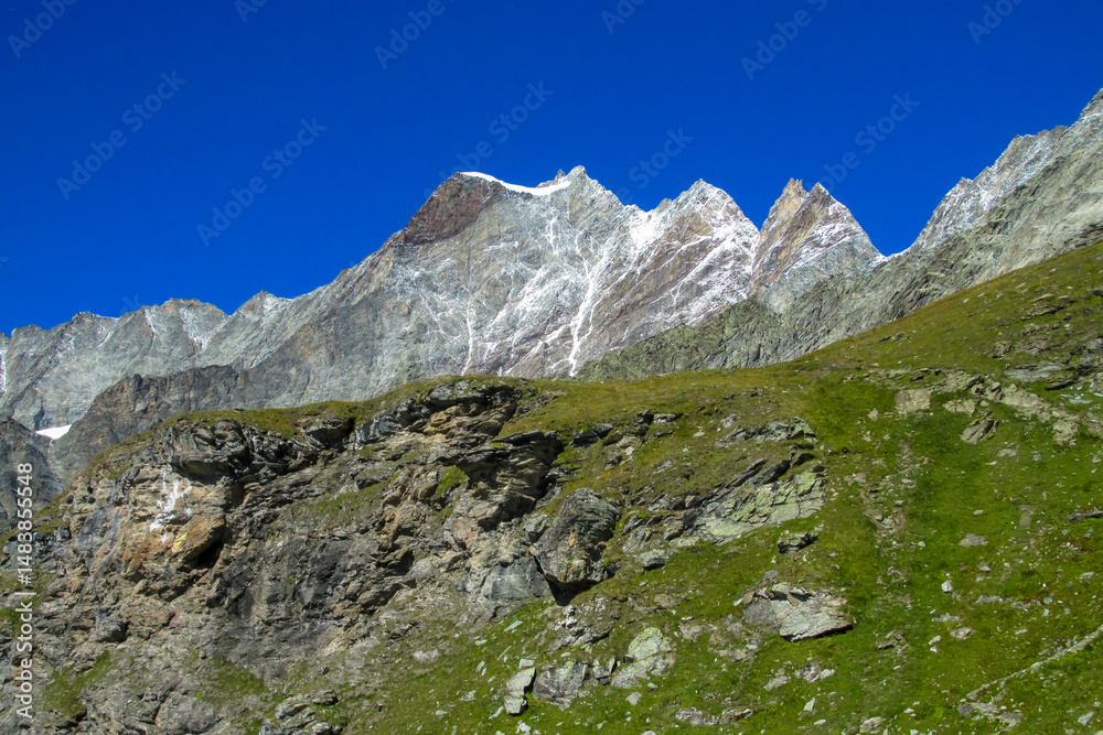 Obraz premium Alps mountains panoramic view in Matterhorn area. Beautiful rocky peaks, mount and gray stones on a sunny day, deep blue sky with clouds. Alps snow mountains Monte Cervino and Monte Rosa range summits