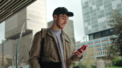 Young man walking while using mobile phone. Happy university student smiling in the city