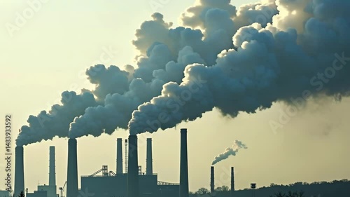 Thick grey smoke billows from industrial chimneys against a hazy sky. Illustrates air pollution climate change and environmental issues