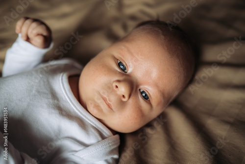 Motherhood and parenthood. Adorable little son lying on brown bed, top view. Cute newborn baby in white infant bodysuit. Adoption and fertility concept.