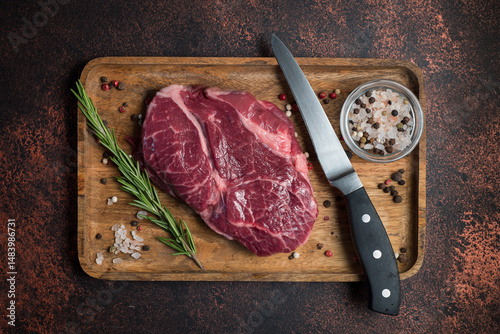 Raw Rib Eye steak with spices on a wooden board on a dark background. View from above.
