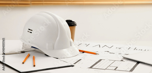 Hardhat with clipboard and house plan on table in constructor's office