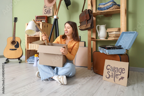 Young woman packing lamp for garage sale in room of unwanted stuff
