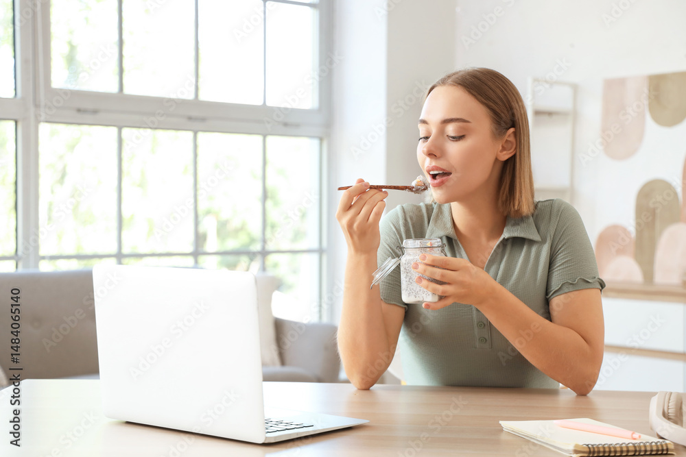 Young woman with laptop eating chia seed pudding at home Young woman with laptop eating chia seed pudding at home