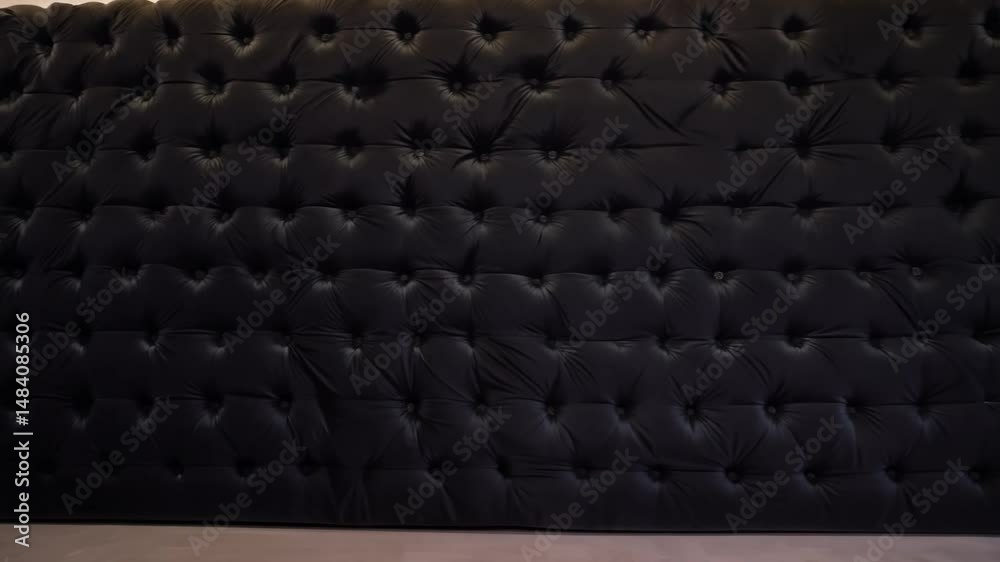 the camera pans right revealing a wall of black velvet fabric with a tufted pattern, creating a textured, luxurious background moody textured surface concept
