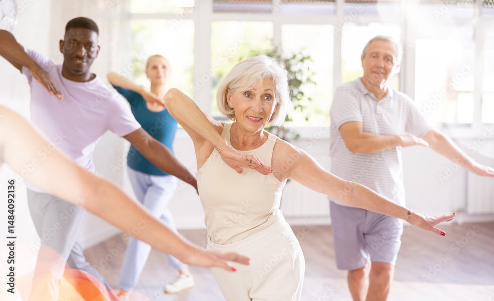 Fototapeta premium Enthusiastic elderly woman practicing modern vigorous dance movements in group dance class for adults