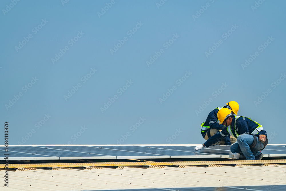Fototapeta premium Two engineers install solar panels on a rooftop, wearing safety gear and helmets. The scene showcases renewable energy, green technology, and sustainable solutions under a clear blue sky.