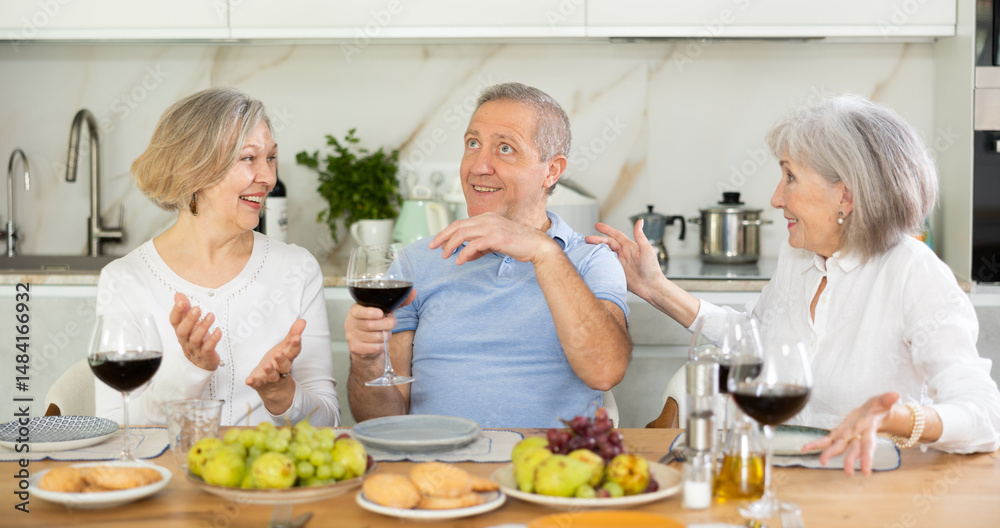 Happy pensioners gathered at the festive table - talking, discussing news and drinking red wine Happy pensioners gathered at the festive table - talking, discussing news and drinking red wine