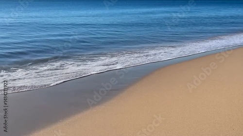 Ocean waves gently washing onto the sandy beach under bright daylight, creating a serene and tranquil coastal scene on a clear day.