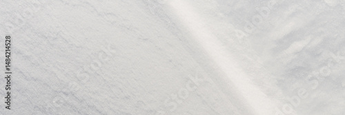 Beautiful winter background with snowy ground. Natural snow texture. Wind sculpted patterns on snow surface. Wide panoramic texture for background and design. Closeup top view with copy space.