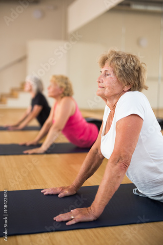 Wallpaper Mural Positive senior lady with group of aged women exercising Hatha yoga poses in modern yoga studio, doing Upward Facing Dog stretching pose. Torontodigital.ca