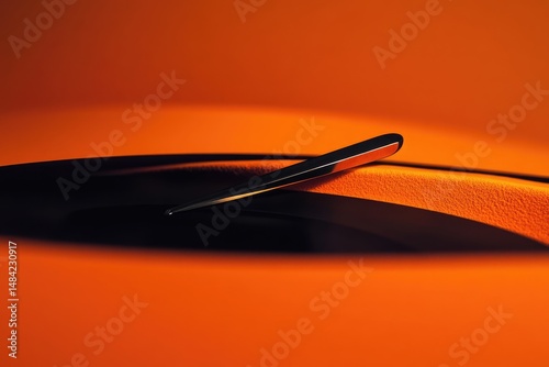 A sleek, metallic object rests on a vibrant orange surface, casting a dramatic shadow.