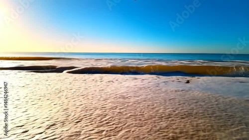 Sandy beach shoreline with ocean waves and blue sky creating a tranquil scene on sunny summer day