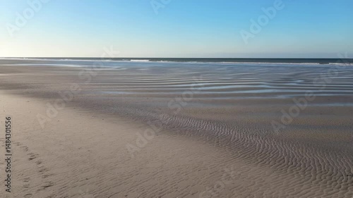 Wide Sandy Beach with Tidal Patterns on a Sunny Day, Clear Blue Sky and Distant Waves