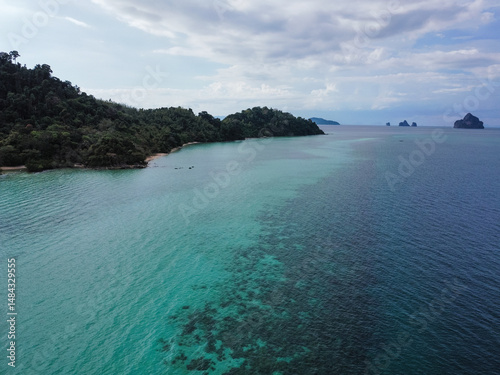 Lush green vegetation covers the hilly coastline, meeting the vibrant turquoise waters under a cloudy sky, creating a serene and picturesque tropical paradise, Ko Kradan, Trang, Thailand photo