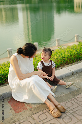Mother enjoying a sunny afternoon by the lake with her toddler, sharing smiles and laughter on a warm day