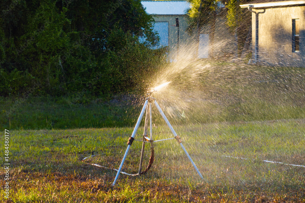 Sprinkler watering lawn grass during dry season Sprinkler watering lawn grass during dry season