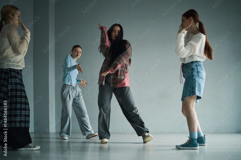 Fototapeta premium Women in casual attire engaging in dance practice in spacious room with concrete floor and walls, moving gracefully and energetically performing various dance moves