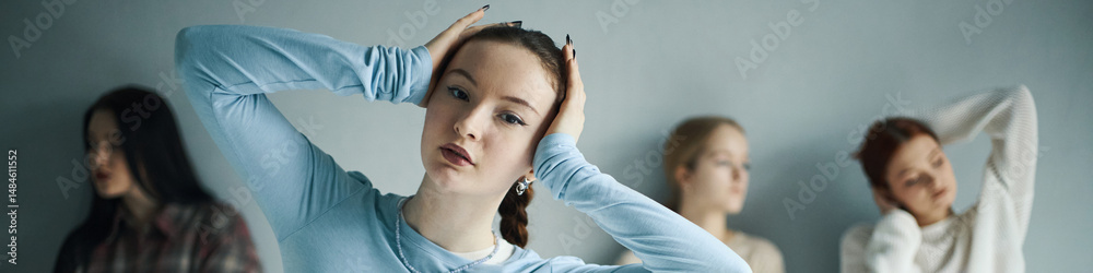 Fototapeta premium Portrait of young woman holding her head while three others are blurred in background, creating a sense of focus and depth in the composition