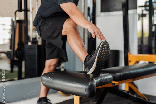 Cuadro en lienzo Closeup of anonymous man doing standing hamstring stretch with one foot raised on a gym bench, wearing athletic shoes
