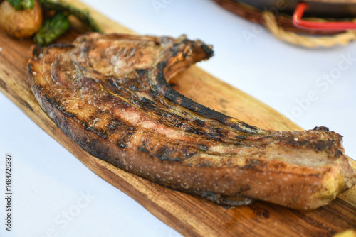 Carne a la parrilla servida en una tabla de madera con verduras asadas.
