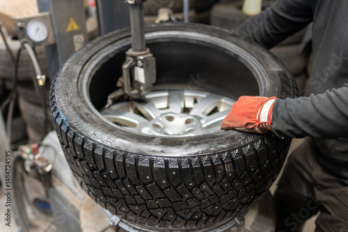 Professional mounting of a studded winter tire on an aluminium wheel in the garage. Seasonal tire change service with specialised equipment.