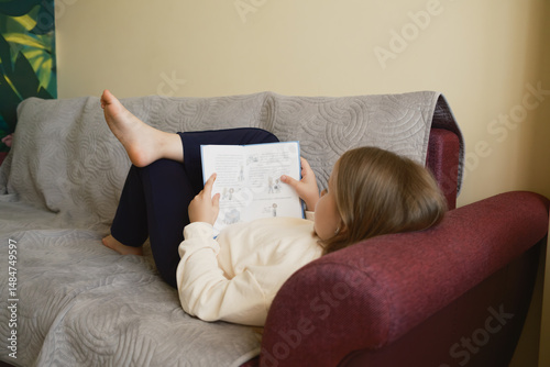 A young girl comfortably reclining on a sofa, immersed in reading a book. The setting emphasizes relaxation, education, and the joy of engaging with stories