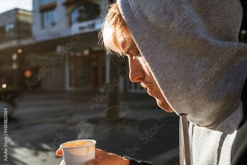 Man in hoodie sipping coffee on cool morning in Manly