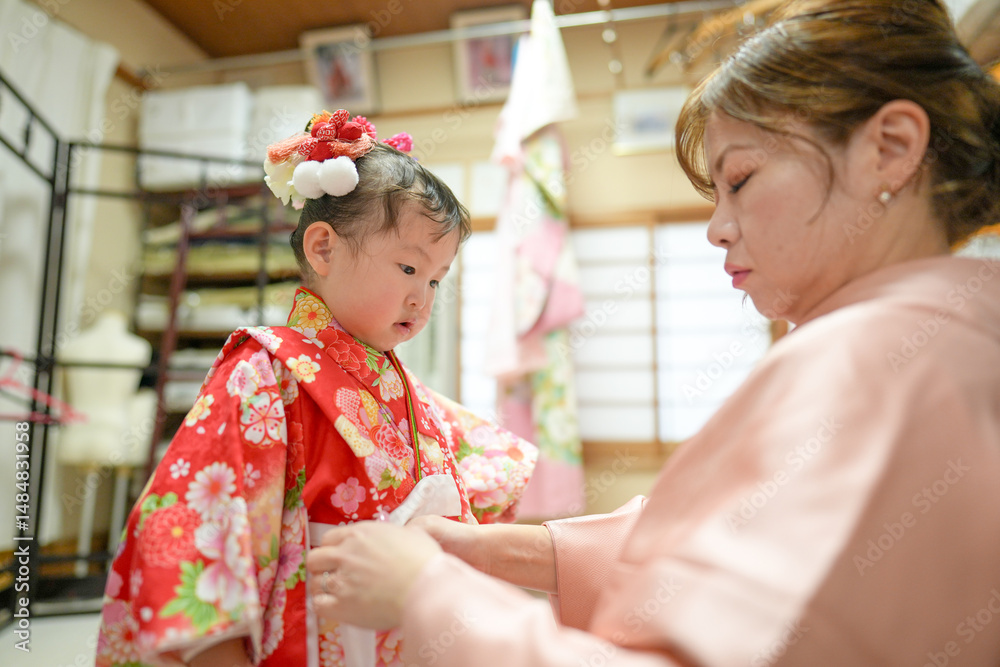Obraz premium A Japanese couple in their thirties, in pink kimonos, help their 3-year-old daughter into her kimono for Shichi-Go-San. This photo captures family love and care before a traditional celebration.