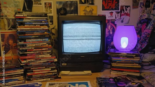 small vintage tv with No Signal screen between stacked CDs with lamp and posters on wall