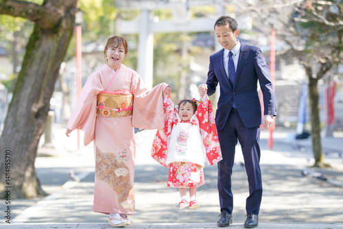 Photography A 3-year-old Japanese girl in a red kimono holds hands with her parents-mom in a pink kimono, dad in a suit-as they jump together for Shichi-Go-San
