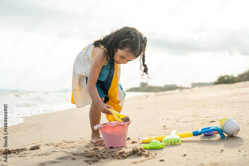 Cheerful adorable little girl having fun outdoor and playing with sand with beach kid toys on the beach in the summer vacation at sunset, happy healthy toddler playful on the tropical seaside. Cheerful adorable little girl having fun outdoor and playing with sand with beach kid toys on the beach in the summer vacation at sunset, happy healthy toddler playful on the tropical seaside.