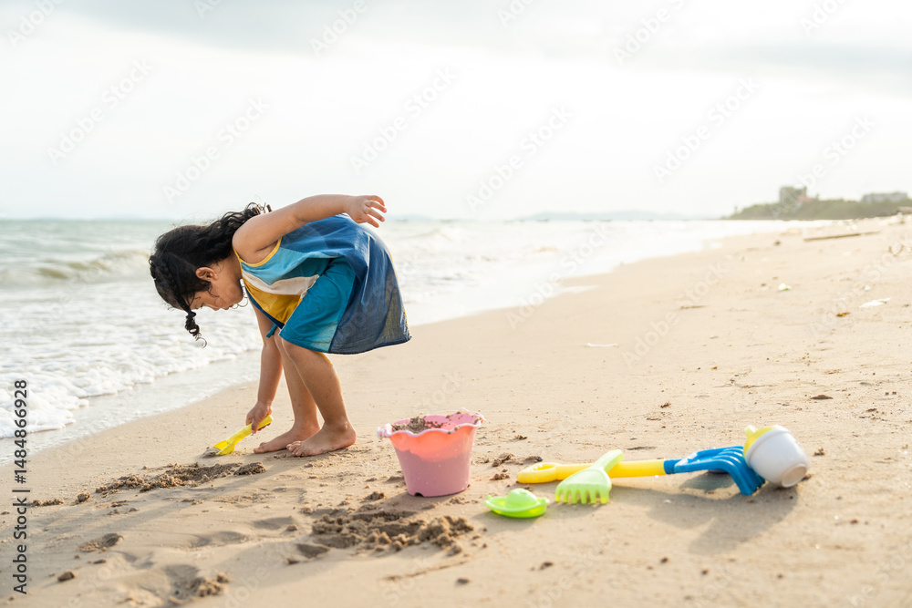 Cheerful adorable little girl having fun outdoor and playing with sand with beach kid toys on the beach in the summer vacation at sunset, happy healthy toddler playful on the tropical seaside. Cheerful adorable little girl having fun outdoor and playing with sand with beach kid toys on the beach in the summer vacation at sunset, happy healthy toddler playful on the tropical seaside.